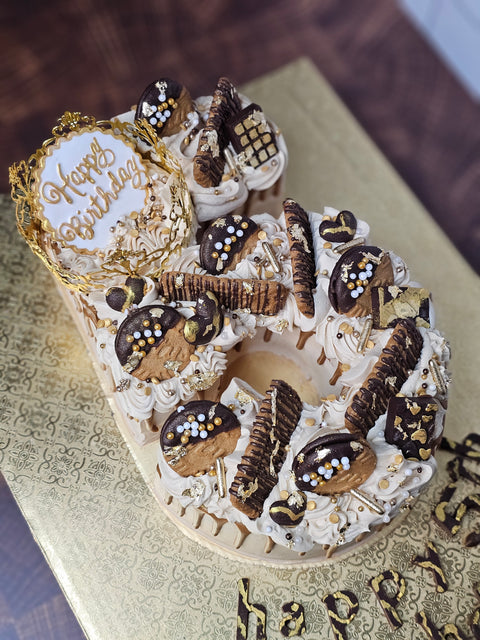Angled picture of a custom buttercream number cake, decorated with biscoff cookies, mini chocolate bars, gold sprinkles and biscoff drip.