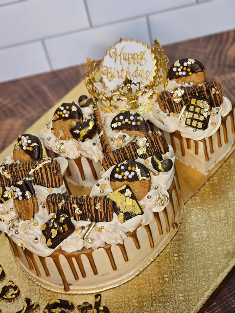 Angled picture of a custom buttercream number cake, decorated with biscoff cookies, mini chocolate bars, gold sprinkles and biscoff drip.