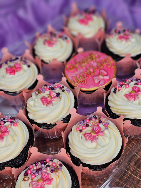 Close up of chocolate cupcakes with white buttercream and pink decorations.