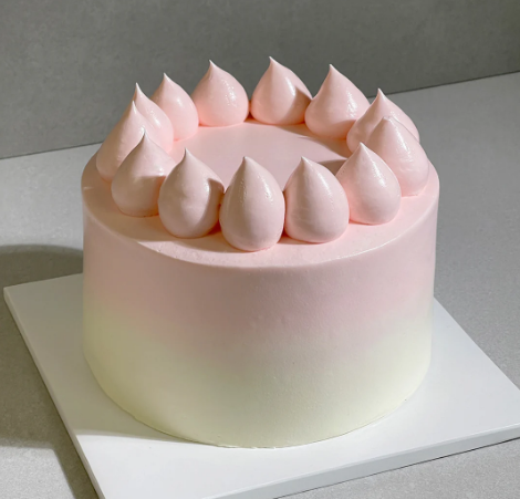 Pink and white ombre buttecream cake on a white cake board.