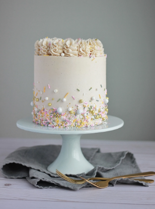 White buttercream cake on a blue pedastal decorated with colorful sprinkles.