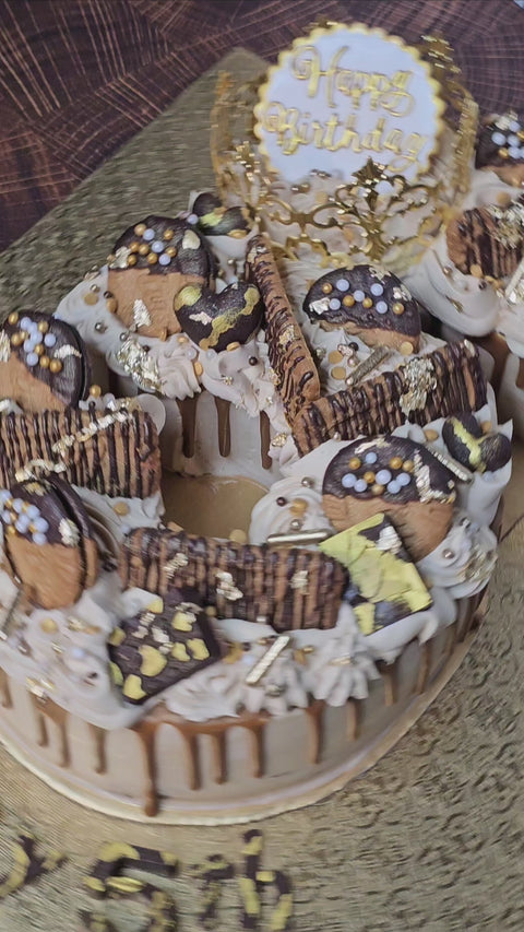 Video of spinning custom buttercream number cake, decorated with biscoff cookies, mini chocolate bars, gold sprinkles and biscoff drip.