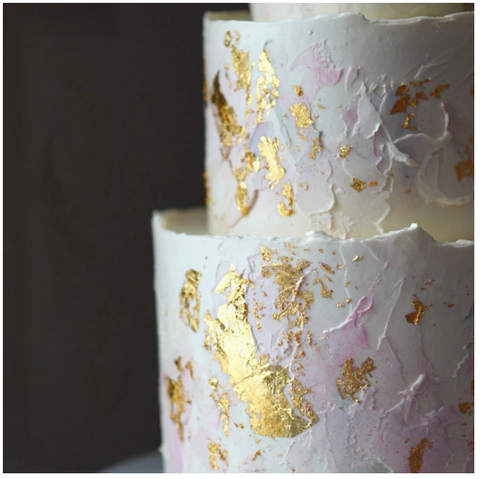 Abstract buttercream cake decorated with white and pink buttercream and gold flakes.