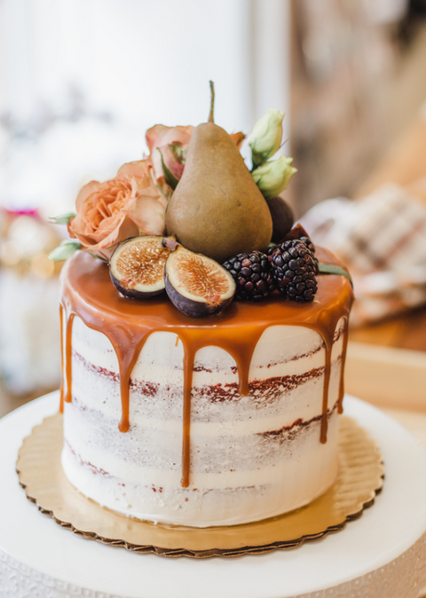 Semi naked white buttercream cake with a caramel drip. Decorated with seasonal fruit and fresh flowers. 