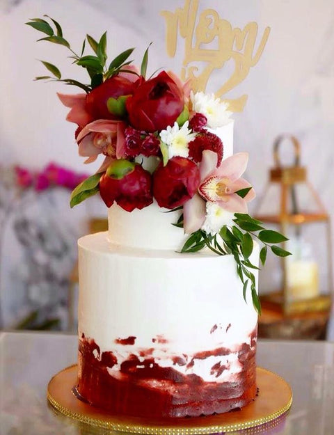 Two tiered white and wine buttercream cake decorated with fall flowers on a gold cake board. 