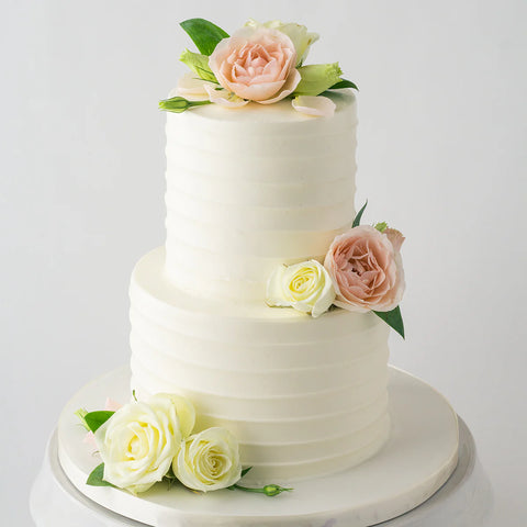 Two tier white buttercream cake decorated with fresh pink and yellow flowers.