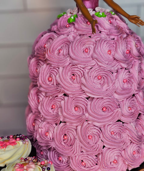 Close up the buttercream skirt of the pink Barbie cake and chocolate cupcakes with pink decorations and white buttercream.