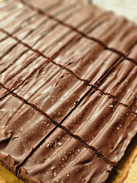 Close up of fudge brownies covered in dark chocolate ganache sprinkled with sea salt.