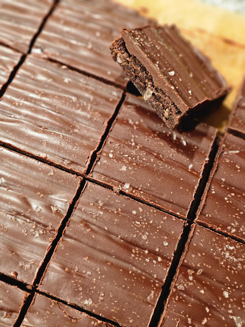 Close up of fudge brownies covered in dark chocolate ganache sprinkled with sea salt.