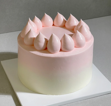 Pink and white ombre buttecream cake on a white cake board. 