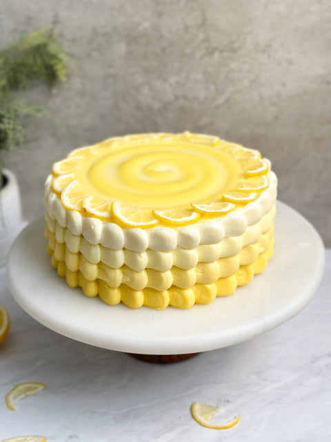 Yellow buttercream cake on a white cake plate.