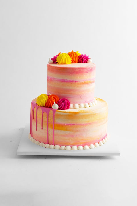 Two tier orange, pink and yellow watercolor buttercream cake on a whote cake board. 