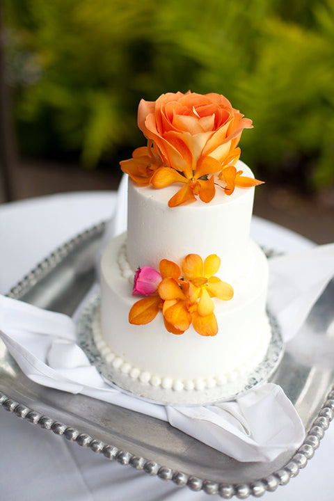 Two tiered white buttercream cake decorated with pink and orange flowers.