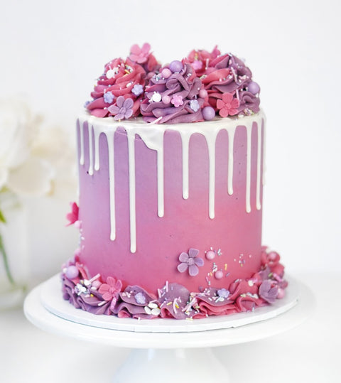 Pink and purple ombre cake decorated with white drip and buttercream swirls.