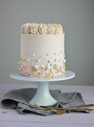 White buttercream cake on a blue pedastal decorated with colorful sprinkles. 