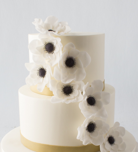 White buttercream cake decorated with gold ribbon and black and white flowers.